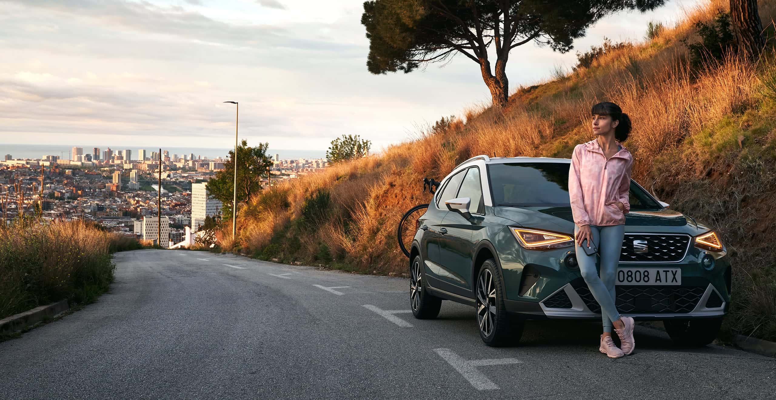 Woman leaning on front grille SEAT Arona dark camouflage colour with white roof