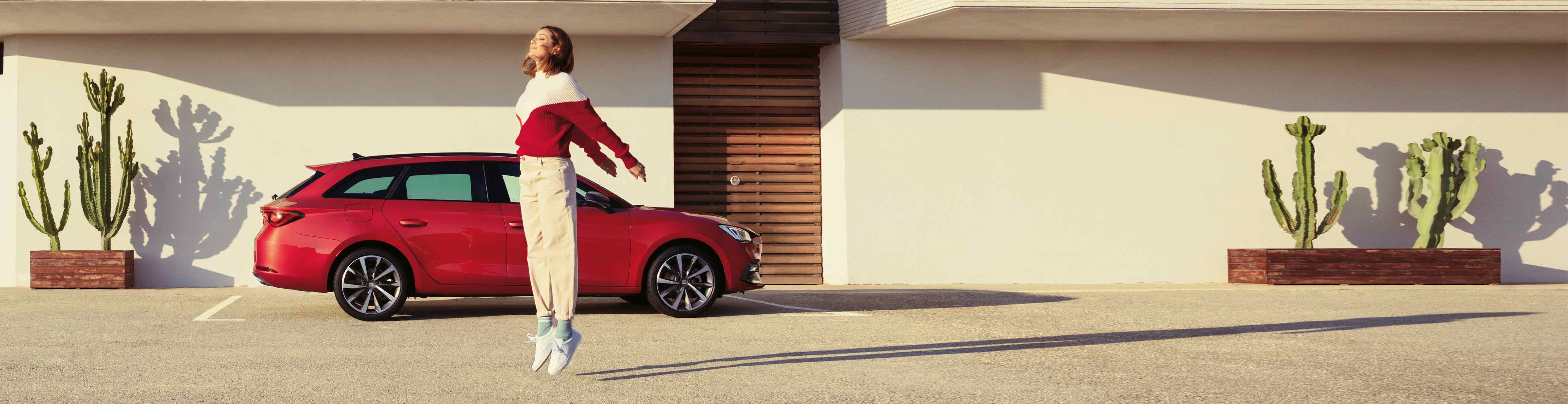 Woman jumping next to SEAT Leon Sportstourer  pure red colour